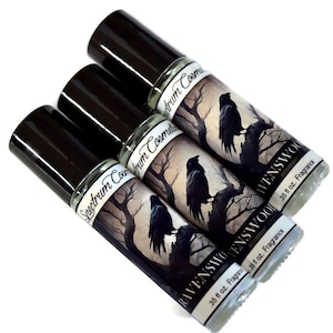 May include: Three glass roll-on fragrance bottles with black caps. Each bottle features a label with a black raven perched on a tree branch against a gray and white background. The label reads "RAVENSWOOD" and "35 fl oz. Fragrance".