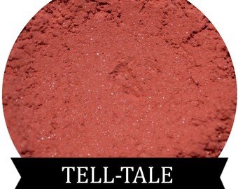 May include: A close-up of a red-toned powder with a fine, shimmery texture. The powder is labeled "TELL-TALE".