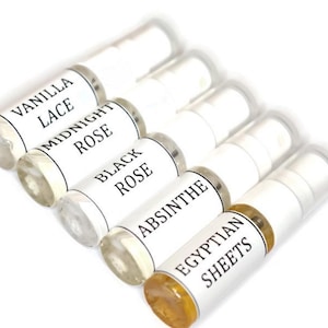 May include: Six small glass bottles with white labels and black text. The labels read "Vanilla Lace", "Midnight Rose", "Black Rose", "Absinthe", and "Egyptian Sheets".