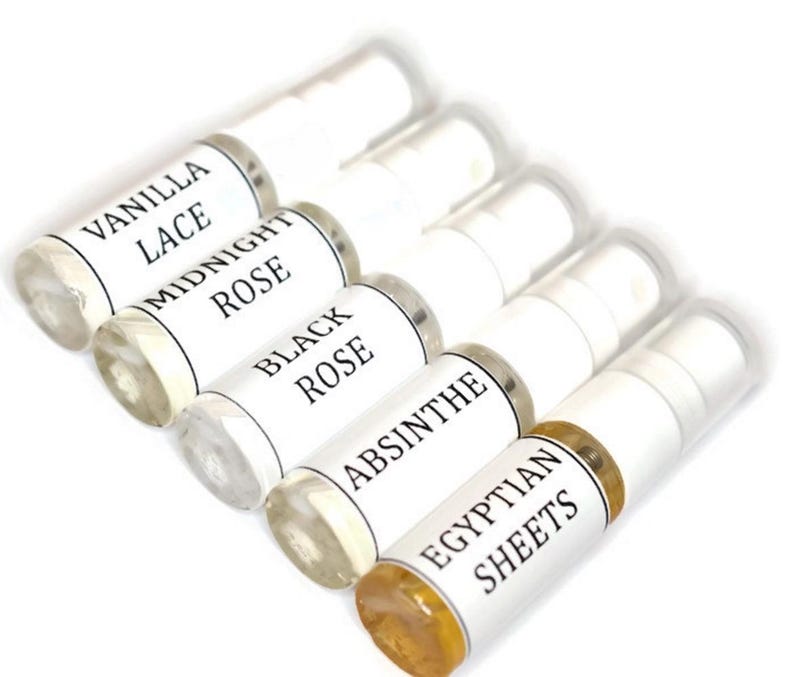 May include: Six small glass bottles with white labels and black text. The labels read "Vanilla Lace", "Midnight Rose", "Black Rose", "Absinthe", and "Egyptian Sheets".