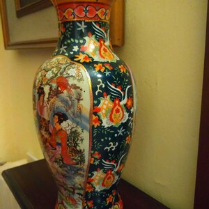 Pu&ograve; includere: Un vaso di ceramica alto e ornato con una base ampia e un bordo svasato. Il vaso presenta uno sfondo verde scuro con motivi floreali e di uccelli, e un pannello raffigurante figure in un paesaggio. Il bordo &egrave; marrone con dettagli rossi e dorati.