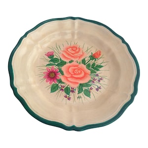 May include: A decorative, off-white ceramic plate with a scalloped edge and a green border. The plate features a hand-painted floral design with pink roses, a pink daisy, and green leaves.