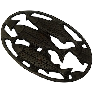 Pode incluir: Trivet ovalado castanho escuro com um design de três peixes. Os peixes estão dispostos em fila, com corpos e barbatanas detalhados. O trivet é feito de ferro fundido e tem uma aparência rústica e vintage.