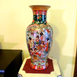 Pu&ograve; includere: Un vaso decorativo in ceramica con una base ampia e un bordo svasato. Il vaso presenta una scena dettagliata e colorata di figure, una tigre ed elementi paesaggistici. La parte superiore e la base hanno accenti rossi e dorati, con una fascia verde scuro.