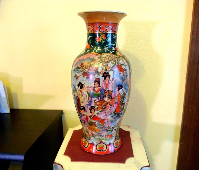 Pu&ograve; includere: Un vaso decorativo in ceramica con una base ampia e un bordo svasato. Il vaso presenta una scena dettagliata e colorata di figure, una tigre ed elementi paesaggistici. La parte superiore e la base hanno accenti rossi e dorati, con una fascia verde scuro.