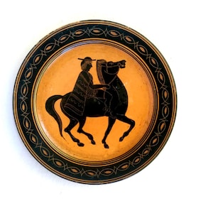 May include: A decorative plate with a black and orange design. The plate features a black silhouette of a person riding a horse, with a black border. The background is orange.