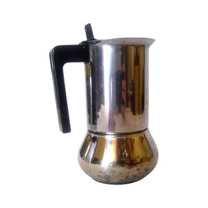Pode incluir: Uma cafeteira de aço inoxidável com acabamento polido e reflexivo. A cafeteira possui uma alça de plástico preta fixada na lateral e uma pequena alavanca preta na tampa superior. A base tem um formato arredondado e bojudo com sinais de uso.