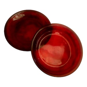 Puede incluir: Dos platos redondos de vidrio rojo con acabado brillante. Los platos tienen un borde ligeramente elevado y un color rojo intenso que se desvanece a un tono más oscuro en el centro. Los platos están sobre un fondo blanco.