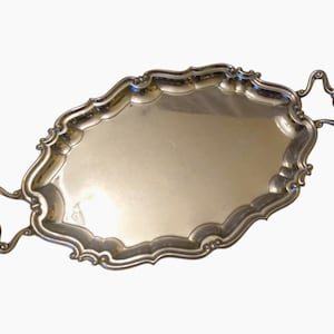 Op de afbeelding: Zilverkleurige ovale serveerschaal met sierlijke, geschulpte randen en decoratieve handgrepen. De schaal heeft een reflecterend oppervlak en is waarschijnlijk van metaal. Een klassiek stuk voor het serveren van eten of het uitstallen van items.