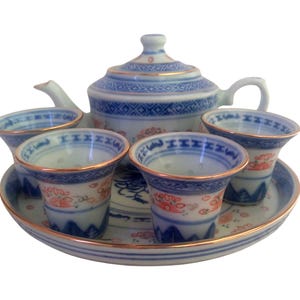 May include: A porcelain tea set with a teapot, four cups, and a serving tray. The set features a blue and white design with gold trim. The cups and teapot have a floral pattern. The tray is round and has a gold rim.