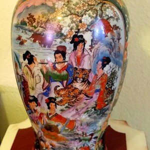 Pu&ograve; includere: Vaso decorativo in ceramica con una pittura colorata e dettagliata di figure asiatiche, una tigre e un paesaggio. Il vaso ha un bordo verde scuro con disegni floreali e una forma arrotondata. L'opera d'arte presenta colori vivaci e dettagli intricati.