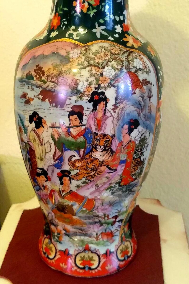 Pu&ograve; includere: Vaso decorativo in ceramica con una pittura colorata e dettagliata di figure asiatiche, una tigre e un paesaggio. Il vaso ha un bordo verde scuro con disegni floreali e una forma arrotondata. L'opera d'arte presenta colori vivaci e dettagli intricati.