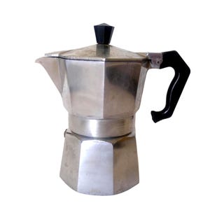 Pode incluir: Uma cafeteira de alumínio prateado para fogão com base octogonal e acabamento polido. Possui uma alça de plástico preta e um botão preto correspondente na tampa articulada, além de um bico vertedor proeminente na seção superior do corpo.
