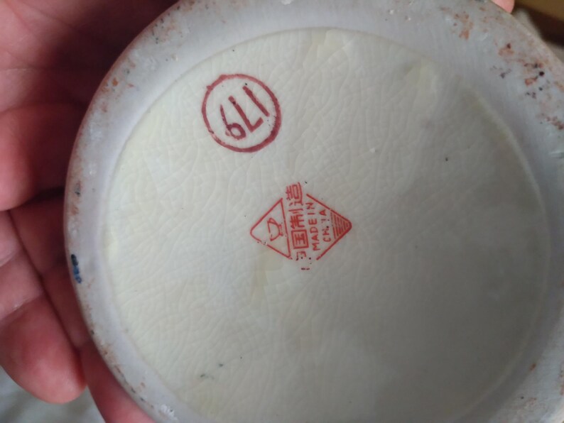 Pu&ograve; includere: Primo piano del fondo di un oggetto in ceramica, probabilmente un vaso o una ciotola. La base &egrave; bianco sporco con un timbro rosso circolare che indica "611". &Egrave; visibile anche un timbro rosso a forma di diamante con caratteri cinesi e "MADE IN CHINA".