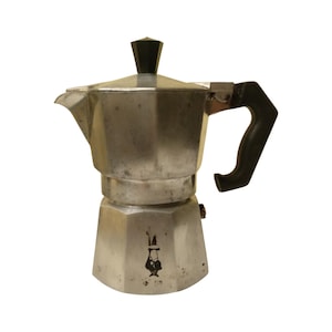 May include: A silver stovetop espresso maker with a black handle and lid knob. The coffee pot has an octagonal design and is made of metal. The handle is curved for easy gripping. The coffee maker is designed to brew espresso.