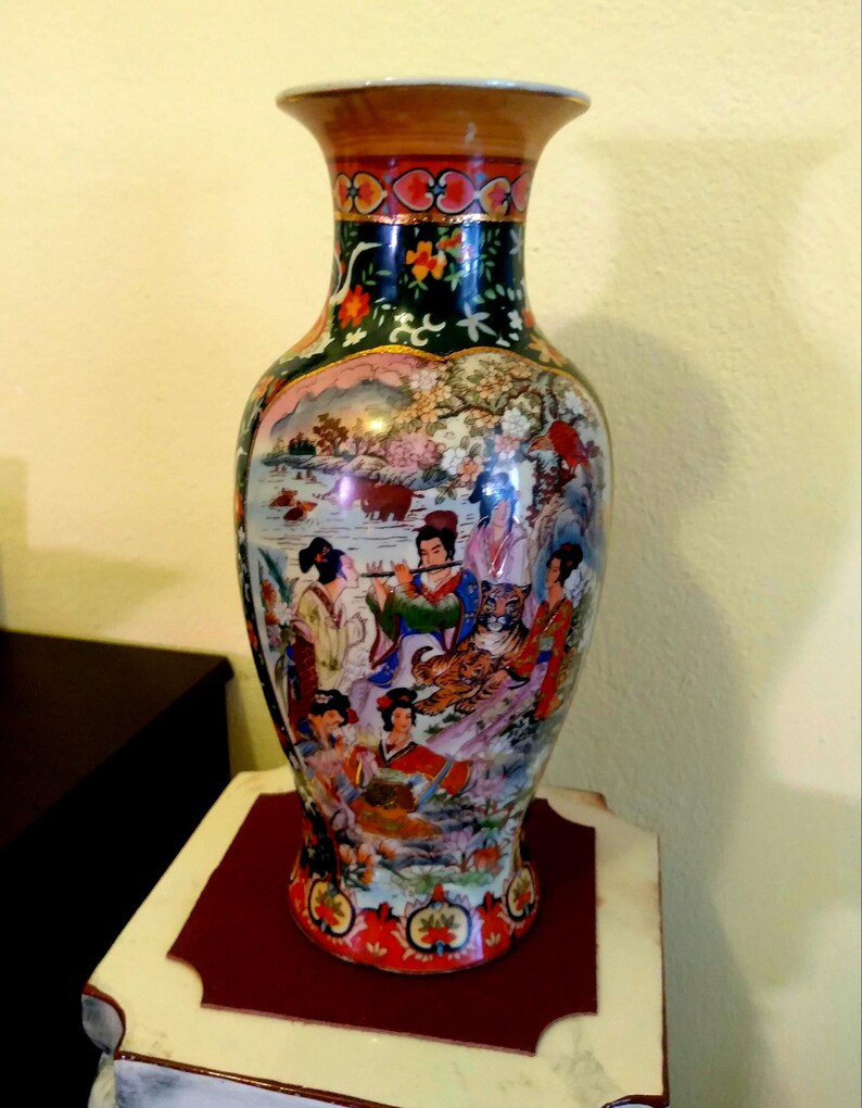 Pu&ograve; includere: Un vaso decorativo in ceramica alto con un design di ispirazione asiatica. Il vaso presenta una scena dipinta con figure, animali e paesaggi dai colori vivaci. La parte superiore e inferiore presentano motivi floreali e geometrici.