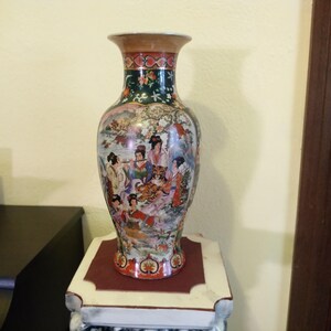 Pu&ograve; includere: Un vaso decorativo in ceramica con una scena dipinta dettagliata di figure e una tigre. Il vaso ha un bordo svasato e un corpo bulboso. I colori includono rosso, verde e oro. &Egrave; esposto su un supporto decorativo.