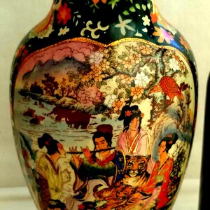 Pu&ograve; includere: Un vaso decorativo in ceramica con una base larga e un collo stretto. Il vaso presenta una scena dipinta dettagliata di figure, animali e paesaggi asiatici in colori vivaci. Il bordo superiore &egrave; dorato e il vaso ha una finitura lucida.