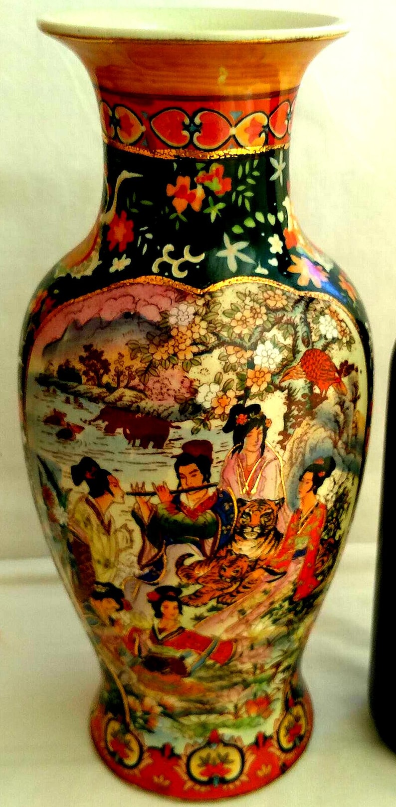 Pu&ograve; includere: Un vaso decorativo in ceramica con una base larga e un collo stretto. Il vaso presenta una scena dipinta dettagliata di figure, animali e paesaggi asiatici in colori vivaci. Il bordo superiore &egrave; dorato e il vaso ha una finitura lucida.
