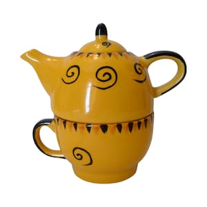 May include: A yellow ceramic tea set for one, consisting of a teapot stacked on top of a matching teacup. Both pieces feature hand-painted black spiral patterns and a decorative border of small black triangles around the rims and lid.