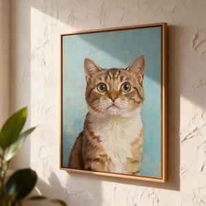 May include: A framed canvas art print featuring a detailed portrait of a tabby cat. The cat has brown and tan fur with a white chest, set against a light blue background. The artwork is in a wooden frame.