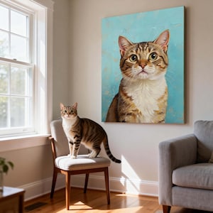 May include: A tabby cat stands on a chair next to a framed canvas art print of a similar cat. The artwork features a close-up of a cat with brown and white fur against a light blue background. The cat in the artwork has large, expressive eyes.