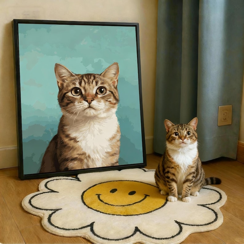 May include: A framed portrait of a tabby cat with a light blue background stands next to a real tabby cat sitting on a daisy-shaped rug with a yellow smiley face. The cat in the portrait and the real cat have similar markings.