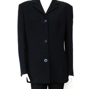 May include: A solid black blazer featuring a notched lapel collar, long sleeves, and a front closure with three dark circular buttons. The garment is displayed on a mannequin, showcasing a structured fit with a straight hemline and two side pockets.