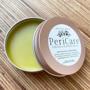 May include: An open, round, metallic tin of PeriCare perineal support salve. The tin is bronze-colored with a white label featuring the product name and ingredients. The salve inside is a light yellow color. The label reads "100% Organic Ingredients".