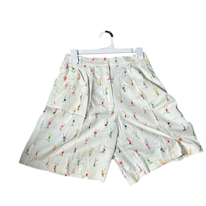 以下が含まれることがあります： カラフルなゴルファーの模様が施された白いコットン製のショートパンツ。ショートパンツはプリーツのウエストバンドとサイドポケットが付いています。