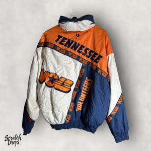 Peut inclure: Veste vintage des Tennessee Volunteers, orange, blanche et bleu marine. La veste affiche le mot "Tennessee" au dos et "VOLS" sur le devant, avec une étoile. Le mot "VOLUNTEERS" est imprimé sur les manches.