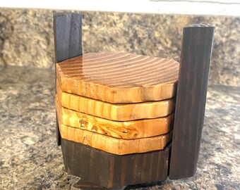 Può includere: Set di quattro sottobicchieri in legno a forma esagonale, impilati e tenuti insieme da un supporto in legno marrone scuro.