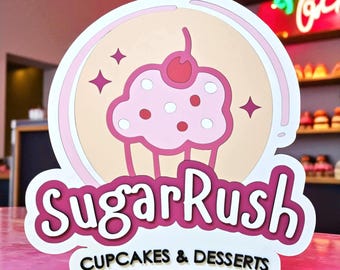 May include: A pink and white sign for "SugarRush Cupcakes & Desserts" featuring a cupcake graphic with a cherry on top. The sign has a layered design with a pink background and white accents. Four star shapes are also included.