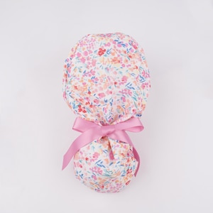 Puede incluir: Un gorro de quir&oacute;fano blanco con un estampado floral rosa y un lazo rosa.