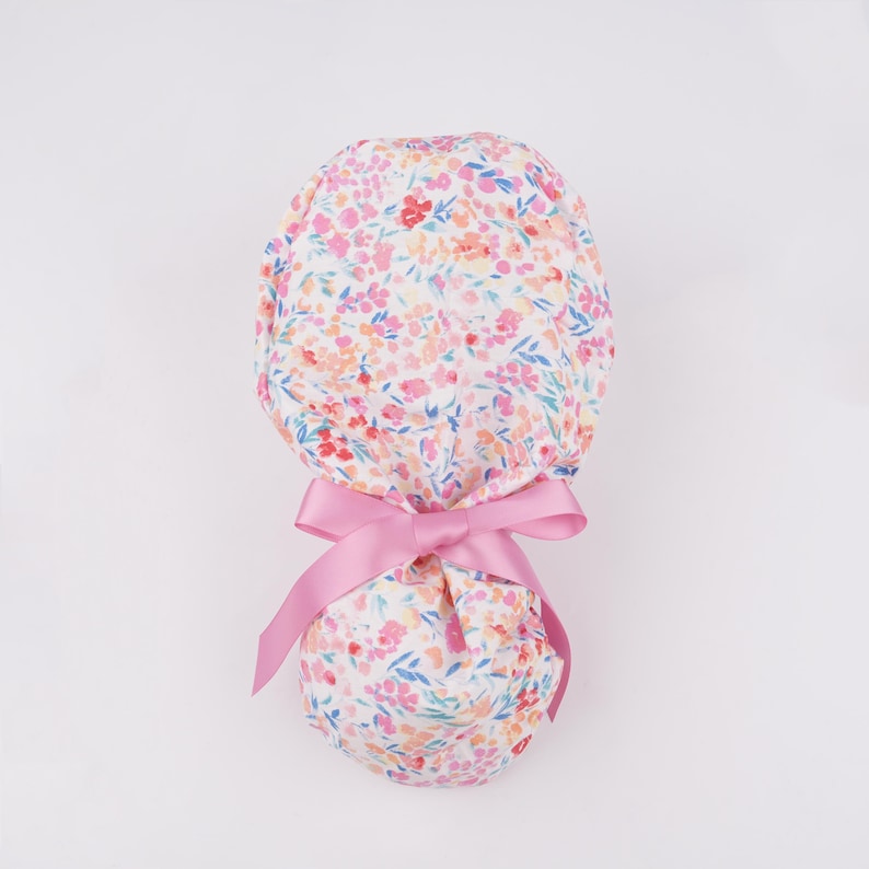 Puede incluir: Un gorro de quir&oacute;fano blanco con un estampado floral rosa y un lazo rosa.