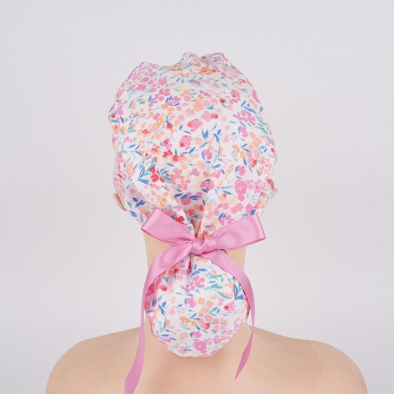 Puede incluir: Una cofia blanca con estampado floral rosa y un lazo rosa. La cofia est&aacute; dise&ntilde;ada para ser usada por profesionales m&eacute;dicos.