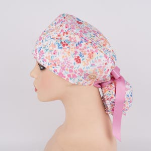 Puede incluir: Un gorro de quir&oacute;fano blanco con estampado floral en tonos rosa, naranja y azul. El gorro tiene un lazo de cinta rosa y un bot&oacute;n en el lateral.