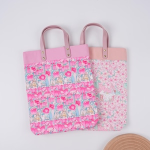 May include: Two tote bags with pink handles and tops. One bag features a pink tulip pattern, and the other has a pink floral design. Both bags have light pink handles and are made of fabric.