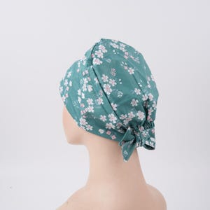 Może przedstawiać: Zielony, chirurgiczny czepek z białym i różowym kwiatowym wzorem. Czepek jest zawiązany z tyłu na kokardę. Zaprojektowany do zakrywania głowy i zabezpieczania włosów, powszechnie używany w środowiskach medycznych.