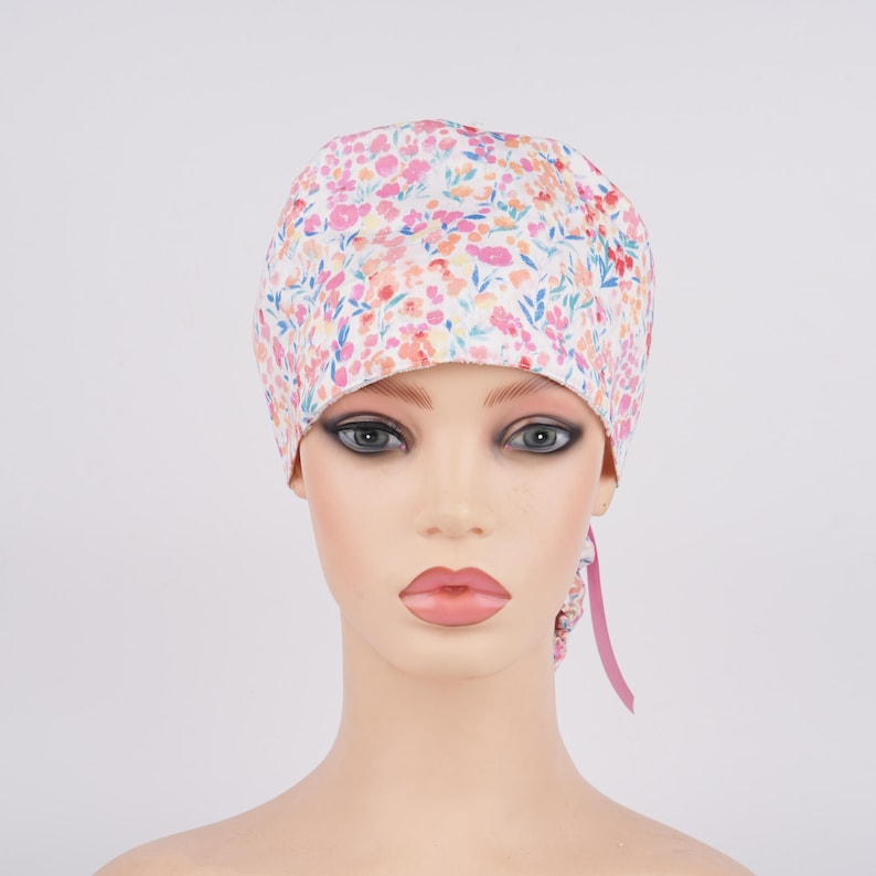 Puede incluir: Un gorro de quir&oacute;fano blanco con estampado floral en tonos rosa, naranja y azul. El gorro tiene una cinta rosa.