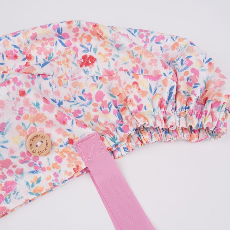 Puede incluir: Un gorro de ducha floral rosa y blanco con una banda el&aacute;stica rosa y un bot&oacute;n de madera que dice "Handmade with Love".