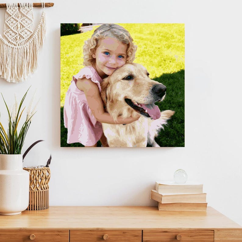 Op de afbeelding: Een vierkante canvas print met een jong meisje met blond krullend haar dat een golden retriever omhelst. Het meisje draagt een roze jurk. De achtergrond toont groen gras en een gele lucht.