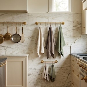 Peut inclure: Une cuisine avec un dosseret en marbre et des armoires crème. Des barres en laiton suspendent des casseroles, des poêles et des serviettes en cuivre de différentes couleurs. Une cuisinière à gaz et un évier sont également visibles.