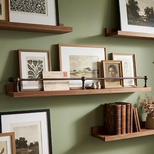 May include: Wooden floating shelves with framed artwork and decorative items. The shelves are mounted on a green wall and hold various framed pictures, small vases, and vintage books. The artwork includes botanical prints and portraits.
