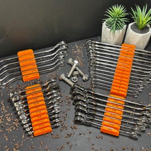 Op de afbeelding: Een verzameling chromen sleutels met oranje maatindicatoren. De sleutels zijn in sets gerangschikt, met bouten en moeren in de buurt. Kleine potplanten staan op de achtergrond.