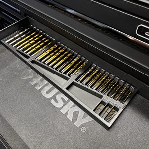 May include: A black tool chest drawer containing a selection of drill bits. The bits are arranged in a black tray, with sizes marked. The drill bits have a gold and silver colour scheme.