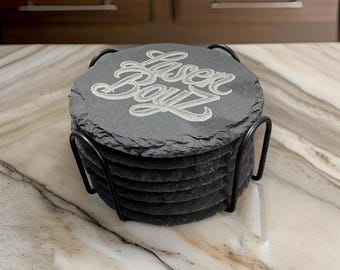 May include: Set of six black slate coasters with a metal holder. The top coaster features the words "Laser Bayz" in a white, cursive font.