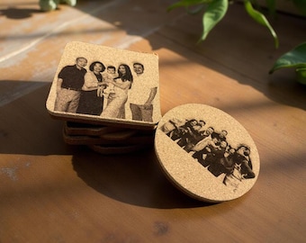 May include: A stack of square coasters and a round coaster with family photos. The coasters are made of a light brown material, possibly cork, with a dark brown image of a family. The coasters are on a wooden surface.