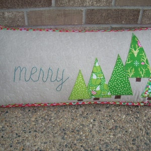 May include: A green and red Christmas cushion with the word "merry" embroidered on it. The cushion features a row of five green Christmas trees with different patterns.