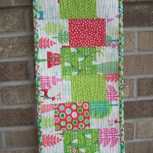 May include: A green, red and white table runner with a Christmas theme. The runner features a variety of patterns, including polka dots, stripes and snowflakes.